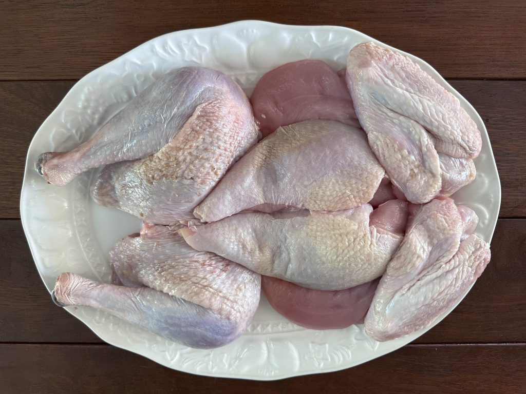 Raw turkey broken down into two legs, two breasts, two wings and the tenderloins on a white platter