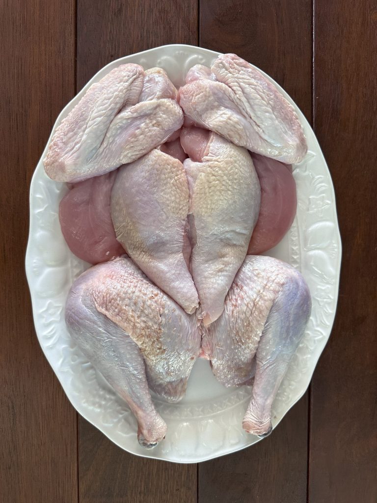 Raw turkey broken down into legs, breasts, wings and tenderloins on a white platter