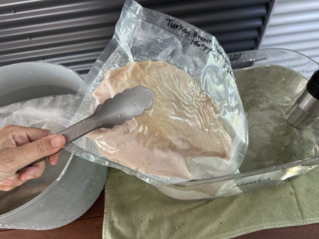 Lifting a cooked turkey breast bag out of the ice bath with tongs