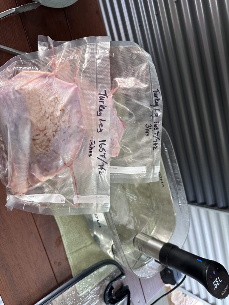 Two vacuum sealed turkey legs labeled 165F / 74C, 3 hrs, next to the sous vide bath